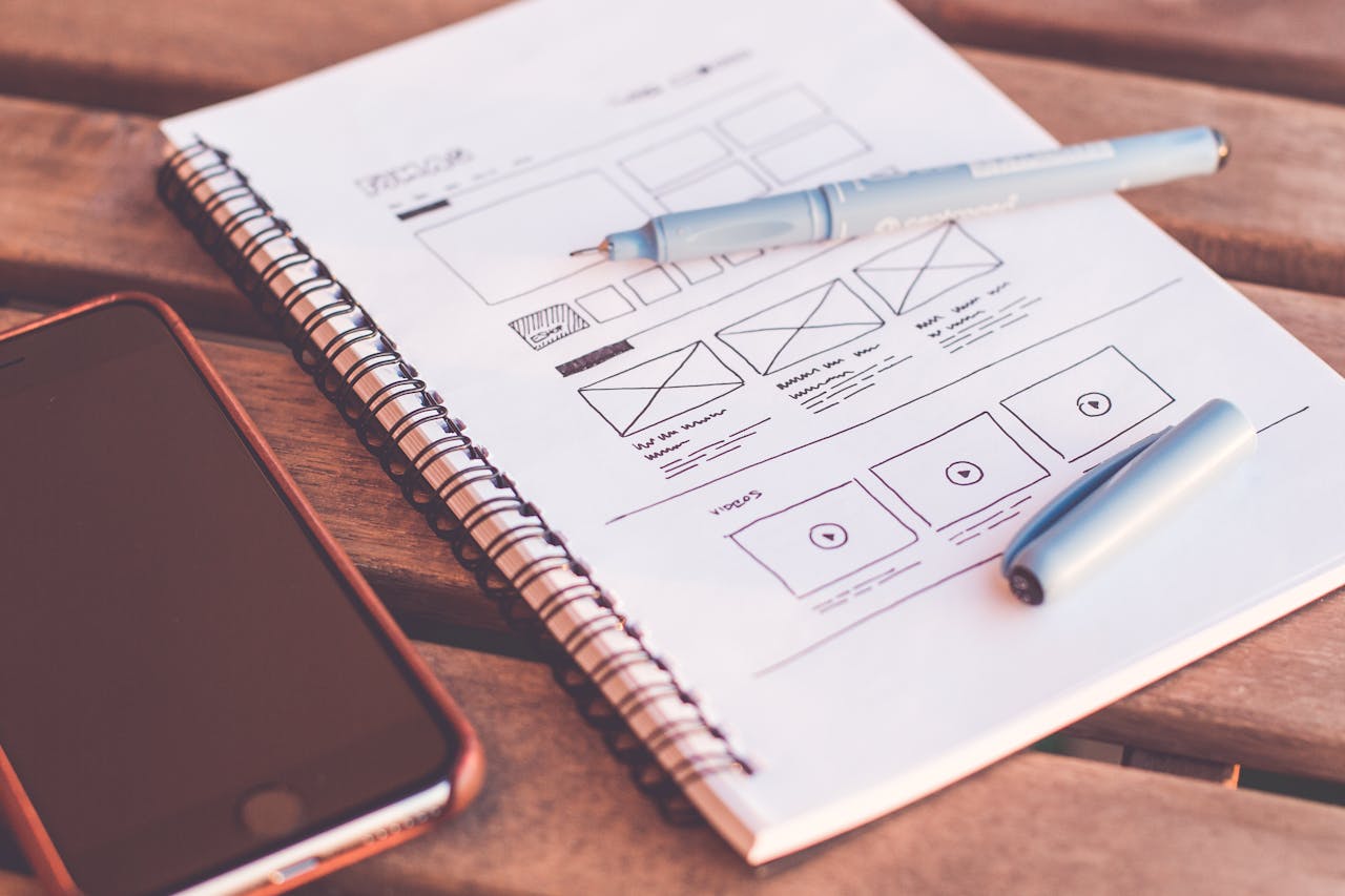 Services Close-up of a notebook with wireframe sketches and a smartphone on a wooden desk.