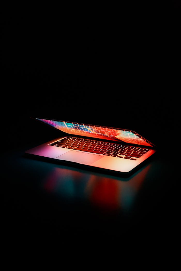 Home Laptop partially opened, emitting vibrant multicolored lights in dark setting.